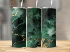 three green and gold marbled metal tumblers with straws in them on a wooden table