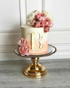 a three tiered cake with pink flowers on top and the letter b on it