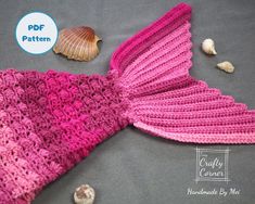 a pink crocheted mermaid tail laying on top of a bed next to shells