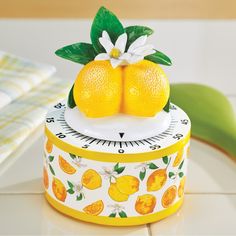 a clock with two oranges on top of it, and a flower in the middle