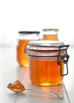 three jars filled with honey sitting on top of a white tile floor next to a spoon