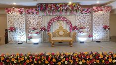 a stage set up for a wedding with flowers on the wall and chairs in front