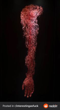 a red sculpture is in the dark with its hands on it's sides and arms stretched out