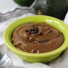 a green bowl filled with chocolate pudding next to an avocado