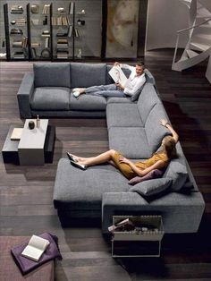 two people lounging on a couch in the middle of a living room with bookshelves