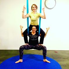 two women doing aerial yoga exercises in an office setting, one on the back of another woman