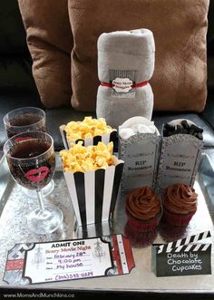 a tray topped with cupcakes and popcorn next to two wine glasses on a couch