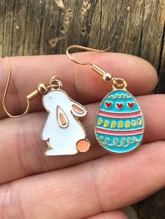 a person is holding two earrings in their hand, one with an easter egg and the other with a rabbit on it