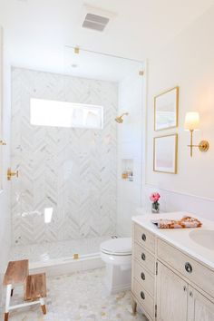 a white bathroom with gold accents and marble counter tops, along with a walk in shower