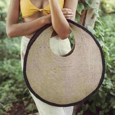 a woman holding a large straw hat in her hands and wearing a yellow top with white pants