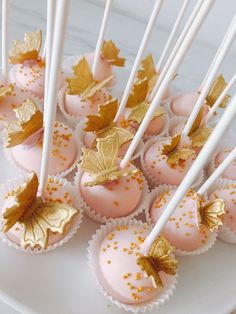 pink and gold cake pops on a white platter with golden leaf decorations, including candles