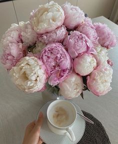 a bouquet of peonies in a vase on a table next to a cup of coffee