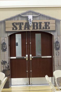 two white chairs sitting in front of a wooden door with the word stable on it