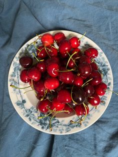 a white plate topped with lots of cherries on top of a blue table cloth