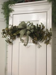 a white door with a green bow hanging from it's side and greenery on top