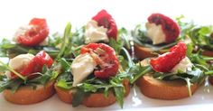 small appetizers are topped with fresh greens and strawberries on toasted bread