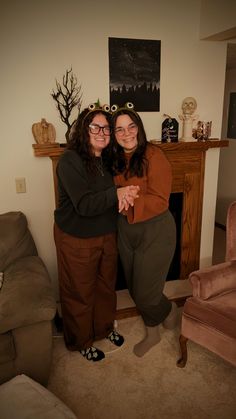 two women standing next to each other in front of a fireplace with their arms around each other