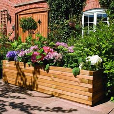 a wooden planter filled with lots of flowers next to a brick wall and door