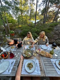 three women sitting at a picnic table with plates of food and drinks on the table