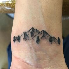 a small tattoo on the wrist of a person with mountains and trees in the background