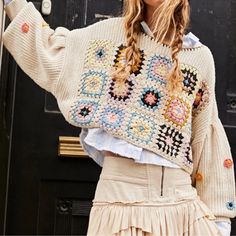 a woman with braids wearing a sweater and skirt standing in front of a door