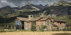 a large stone house in the middle of a grassy field with mountains in the background