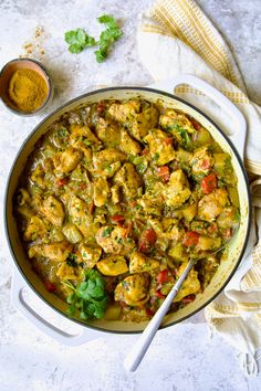 a pan filled with chicken and vegetables on top of a white table next to a spoon