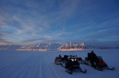 two people on snowmobiles in the middle of nowhere with mountains in the background