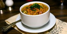 a white bowl filled with soup sitting on top of a plate next to a spoon