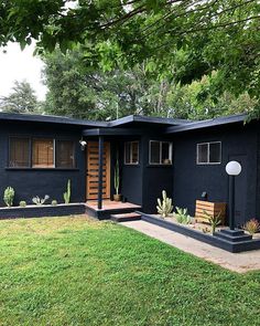 a small black house with cactus plants in the front yard and trees on either side