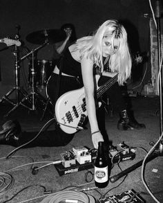 black and white photograph of a woman playing the bass guitar in front of other instruments