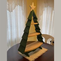 a wooden christmas tree sitting on top of a table next to a curtained window