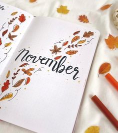 an open notebook with the word november written on it next to autumn leaves and pumpkins