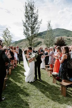 a bride and groom kiss as they walk down the aisle at their outdoor wedding ceremony