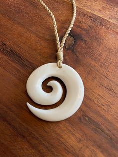 a white necklace with a spiral design hanging from it's side on a wooden table