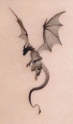 a dragon tattoo on the back of a woman's shoulder, with its wings spread out