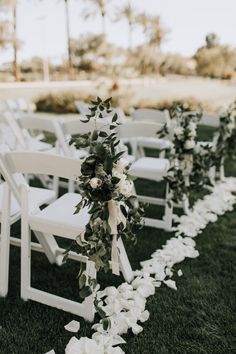 an aisle with white flowers and greenery is lined up on the grass for a wedding ceremony