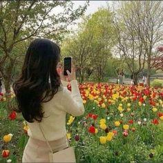 a woman taking a photo of flowers in the park with her cell phone while wearing a sweater