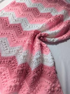 a pink and white crocheted blanket laying on top of a bed next to a pillow