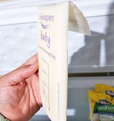 someone holding up a baby milk carton in front of a refrigerator door with the label on it