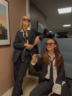 two women dressed in business attire posing for the camera while one holds a wine glass