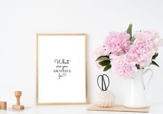 pink flowers are in a vase next to a white wall with a framed print on it