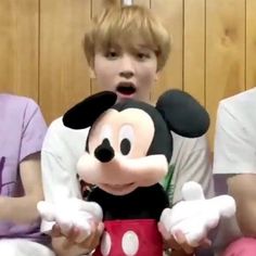 a young boy is holding a mickey mouse stuffed animal in front of two other children