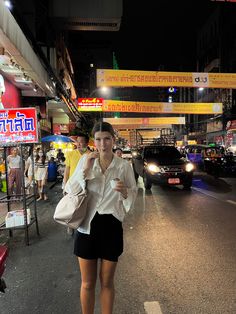 a woman is walking down the street at night with her hand in her pocket and holding a cell phone to her ear