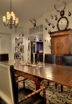 a large wooden table surrounded by black leather chairs and deer heads on the wall behind it