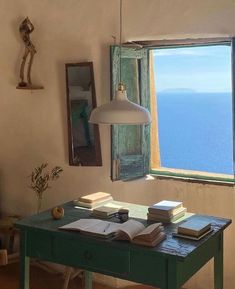 an open book on a table in front of a window with the ocean seen through it