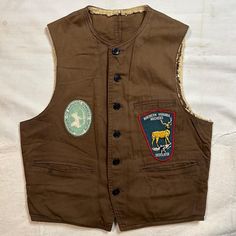 International Shipping Available!! This is a killer 1940s Windward Vest with Bow Hunting Patches. This vest is in distressed vintage condition with spots throughout as shown. The shearling lining of this vest has crumbled. This would be a great option to re-line with a camp blanket or something like that. This fits around a mens size S/M but please refer to all pictures and measurements before buying since all sales are final. Measurements taken while laying flat. 21 inches pit to pit.  22 inches from top of collar to bottom down back. Front is a couple inches longer.  Since all sales are final, I am happy to answer any questions you may have to ensure you know exactly what you are getting. Also, feel free to contact me for international shipping prices! Brown Cotton Vest With Button Closure, Retro Brown Cotton Vest, Vintage Cotton Vest With Button Closure, Brown Cotton Vest With Buttons, Vintage Workwear Vest Outerwear, Vintage Workwear Vest With Pockets, Vintage Vest With Pockets For Work, Vintage Workwear Vest With Buttons, Vintage Vest With Buttons For Workwear