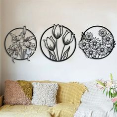 three metal flowers are hanging on the wall next to a yellow couch and white pillows