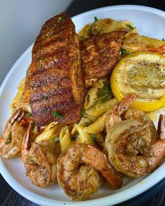 a white plate topped with shrimp, pasta and lemon wedged meat next to a slice of lemon