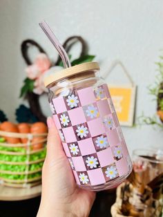 a hand holding a pink and white flowered mason jar with a straw in it